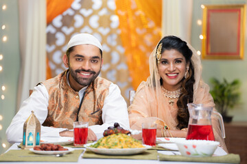 Happy smiling indian muslim couple by looking camera during ramadan dinner festival celebration at home - concept of family bonding, traditional culture and ramadan