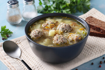 Soup with turkey meatballs, noodles and vegetables in dark bowl on blue background, Closeup