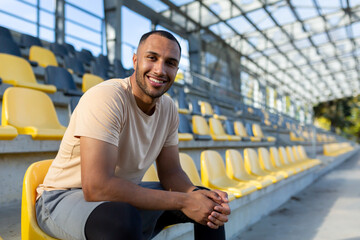 Portrait of young athlete in stadium, man sitting on chair smiling and looking at camera close up, runner resting from training and fitness - Powered by Adobe