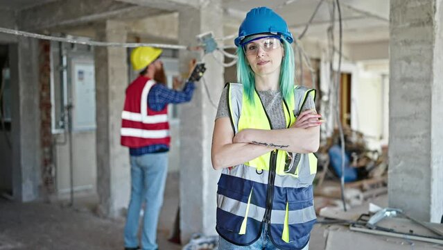 Man and woman builders standing with arms crossed gesture working at construction site