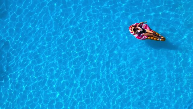 Relaxed girl on an inflatable mattress in the pool in the summer relaxes and swims, shot from above by a drone