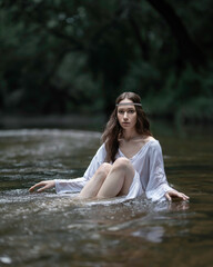 A girl in a Slavic white shirt bathes in a forest river