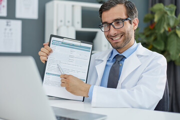 Close up of a doctor and patient hands while phisician pointing into medical history form at clipboard