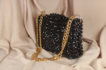 Handmade black bead bag with gold handle on fabric. Selective focus. 