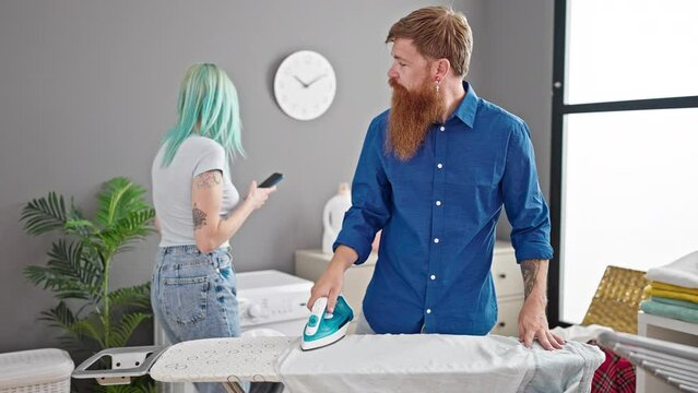 Man and woman couple ironing clothes while girlfriend use smartphone at laundry room