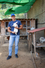 A male farmer holds a white rabbit in his hands on an open farm.