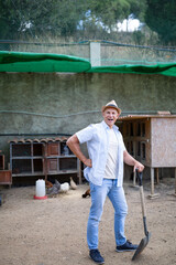 A man holds a shovel in his hands in an open rabbit farm.