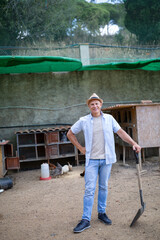 A man holds a shovel in his hands in an open rabbit farm.