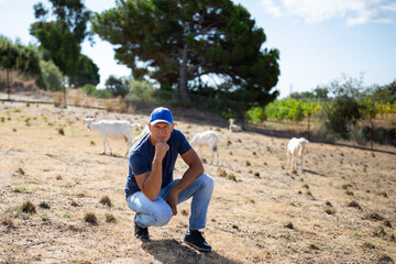 The farmer stands in front of walking goats.