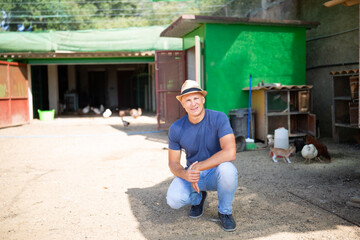 A male farmer leans on a shovel in an open rabbit farm.