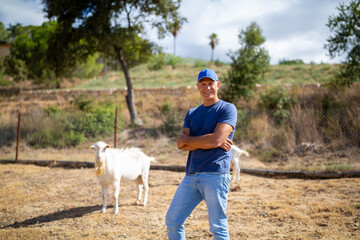 The farmer stands in front of walking goats.