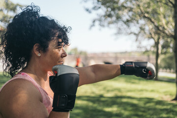 Female athlete with street boxing gloves throwing a front punch during her training. Side view.