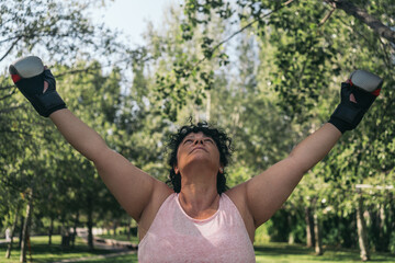 Female athlete with street boxing gloves raising her arms to the air in sign of strength or victory during her training.s