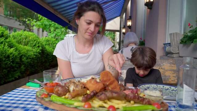 Mother and child eating an abundant Greek plate of food at restaurant table, people dining a generous feast