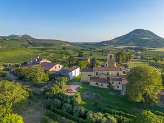 Old church in small rural village in the countryside in Italy in front of vast Italian green vineyard rolling hills landscape in summer
