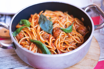 Spaghetti with meatballs, tomato sauce and basilic, popular italian pasta dish served in a pan.