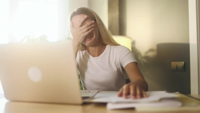 Worried nervous young businesswoman freelancer crying having problems with paper work document at light home Stressed self employee feeling exhausted and looking at screen with sad face at workplace