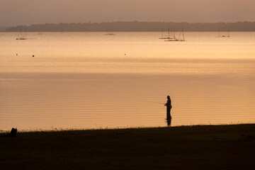 Silhouette of a man standing fishing in the lake at sunrise.