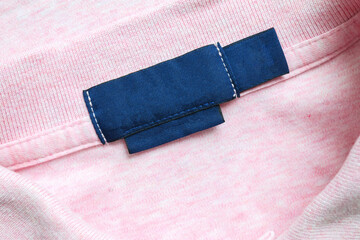 Blank blue laundry care clothes label on pink shirt fabric texture background