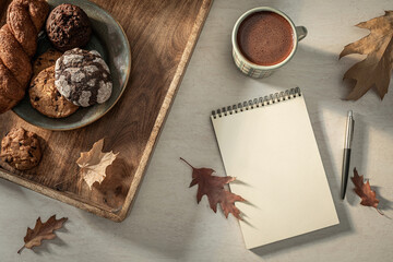 Blank notebook page, pen and mug of hot chocolate on the desk in cozy autumn scenery