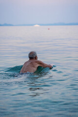 Aged man swims in the Adriatic sea. Gray haired man swimming in tranquise water of sea an sunset time.