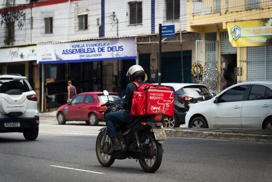 Salvador, Bahia, Brazil - August 11, 2023: A food delivery person using the ifood app is seen riding his motorcycle on Avenida Bonoco