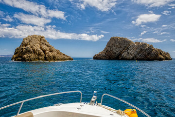 the bow of a boat anchored in front of two rocks at a yellow buoy under a sunny blue sky