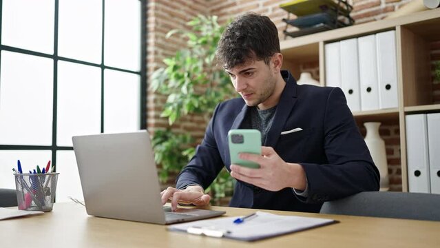 Young hispanic man business worker using laptop and smartphone at office