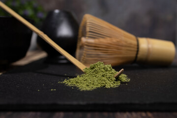 matcha tea black bowl with gray stains gray whisk and bamboo spoon on table with cane tablecloth with old green tea old green tea cement background with stains foreground photo of diner view with spac
