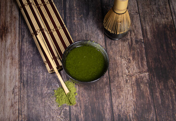tea matcha black bowl with gray stains whisk and bamboo spoon on wooden table with tea green powder on top and a rolled cane tablecloth photo of diner close-up with space for text 