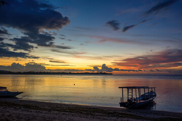 A colorful sunset at Gili Air beach in Indonesia. Calm sea, blue evening sky, red-orange sky and silhouettes of people