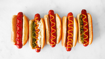 Variety of unique hot dogs with an assortment of toppings. Overhead view on a white marble...