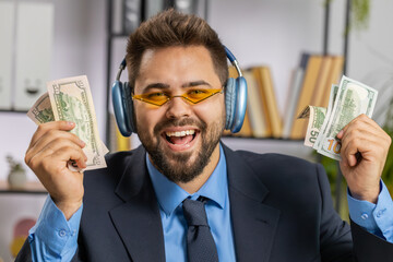 Caucasian businessman holding fan of cash money dollar banknotes celebrate, dance, success career, lottery jackpot game winner, big income, wealth at home office workplace desk. Remote distant working