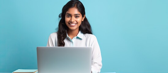 Smiling Indian teen girl using laptop for online study on blue background Happy student in educational webinar
