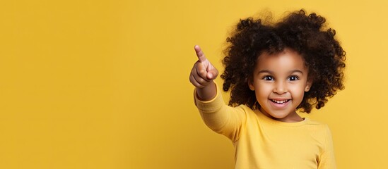Smiling little girl giving a thumbs up indicating a blank space for advertising Studio photo on yellow backdrop