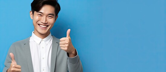 Smiling Asian man points at copy space on blue background with phone