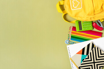 Back to school, education concept Yellow backpack with school supplies - notebook, pens, eraser rainbow, numbers isolated on green background