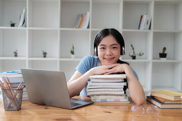 Young smiling Asian student laying down her head on the stack of books, relaxing after the study.