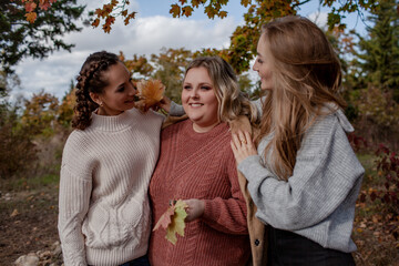 Multiracial female people  with different bodies and hairs walking in the fall parks together.  Friends wearing warm fashion clothes, knitted sweaters.