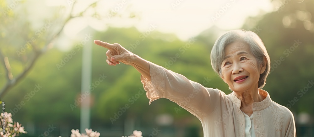 Canvas Prints Elderly Asian woman in her 60s happily pointing upward in a park