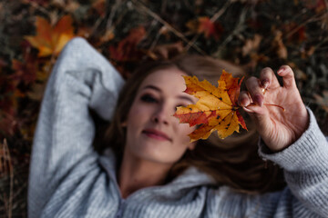 Portrait of a beautiful woman  hold the fall leaves and resting in the park. The happy girl wearing...