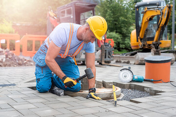Laying interlocking paving. A worker is placing interlocking paving stones around the sewer manhole...