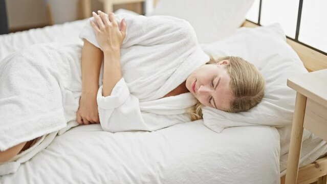 Young blonde woman suffering for menstrual pain lying on bed at bedroom
