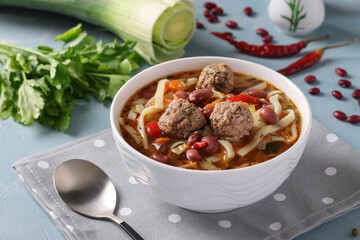 Asian spicy soup with meatballs, beans and noodles on white bowl on blue background
