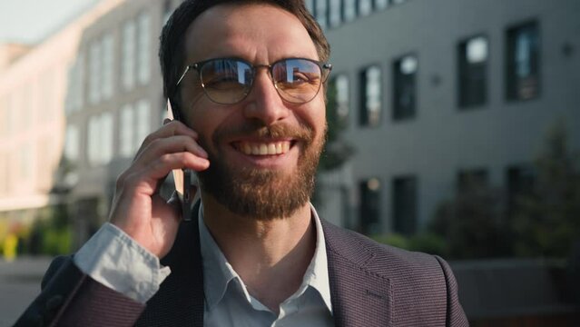 Cheerful happy Caucasian man talking mobile phone in city carefree conversation outside businessman smile talk with business partner smartphone call laughing communicate outdoors near office company