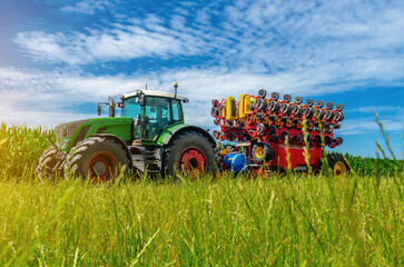 Large tractor on summer field. Low angle view through grass to tractor. Agricultural landscape