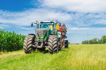 Agricultural summer bright landscape. Large seeder near corn field against a background of clouds.