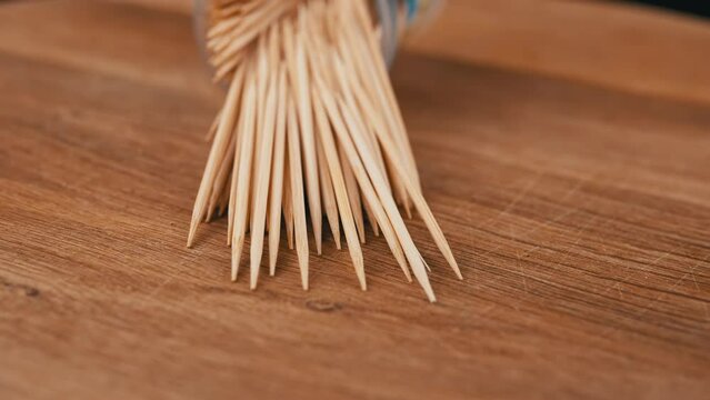 Scattered Toothpicks Rotate on a Wooden Background. Close up. A set of bamboo wooden toothpicks in a plastic cup. Home oral care after meals. Teeth cleaning. Blurred motion. Dentistry concept. Loop.