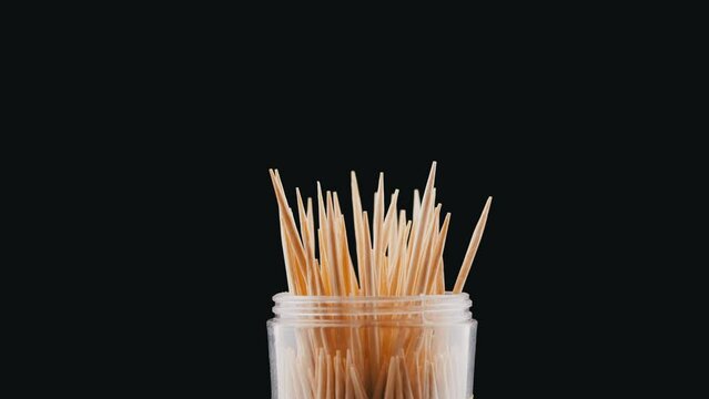 Wooden Toothpicks Rotate on a Black Background. Close up. A set of bamboo toothpicks in a transparent plastic cup. Home oral care after meals. Teeth cleaning. Blurred motion. Dentistry concept. Loop.