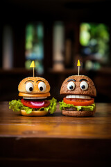 Hamburgers with cheese, lettuce, tomato and eyes on a wooden table. Food character.